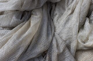 Nahaufnahme eines drapierten, strukturierten, halbtransparenten Stoffes mit einem netzartigen Muster in Grau- und Cremetönen.