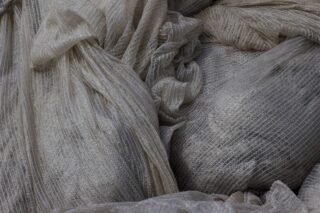 Nahaufnahme mehrerer locker drapierter, strukturierter, heller Stoffbahnen mit sichtbaren linearen Mustern und Falten.