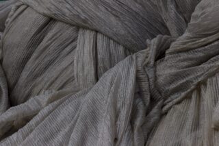 Nahaufnahme eines hellgrauen Plisseestoffs mit strukturierten, gekräuselten Falten und überlappenden Lagen.