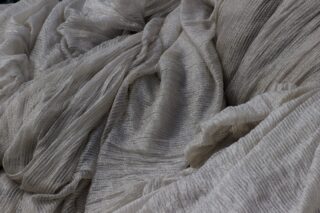 Nahaufnahme eines hellgrauen, zerknitterten, durchsichtigen Stoffes mit einem gestreiften, strukturierten Muster.