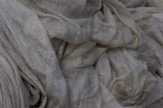 Nahaufnahme eines hellgrauen, transparenten Stoffes mit gekräuselter Textur und horizontalen Linien, locker gerafft und geschichtet.