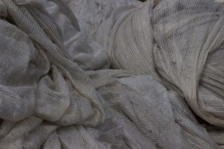 Nahaufnahme eines locker gestapelten, hellgrauen Netzgewebes oder Netzes mit sichtbaren Strukturmustern und Falten.