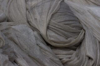 Nahaufnahme mehrerer Lagen hellgrauen, strukturierten Stoffes mit einem leicht glänzenden, gerippten Muster, gefaltet und überlappend.