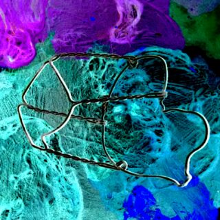 Ein gedrehter Drahtkäfig aus einem Champagnerkorken liegt auf einem strukturierten, abstrakten Hintergrund in Grün-, Blau- und Lilatönen.