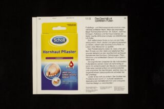 Ein aufgeschlagenes Buch, das auf der linken Seite eine Packung Scholl Hornhaut Pflaster Fußpflaster und auf der rechten Seite einen deutschen Text über Fußpflegeprodukte zeigt.