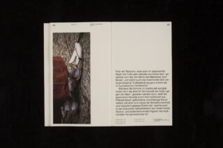 Offenes Buch auf schwarzem Hintergrund; die linke Seite zeigt eine Nahaufnahme von gebundenen weißen Schuhen und rotem Stoff, die rechte Seite enthält deutschen Text mit größtenteils leerem Raum.