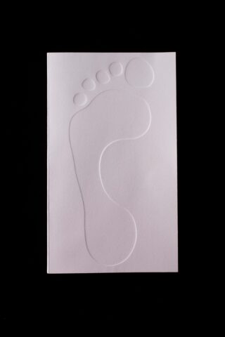 Ein weißes Blatt Papier mit der geprägten Umrisslinie eines menschlichen Fußabdrucks auf schwarzem Hintergrund.