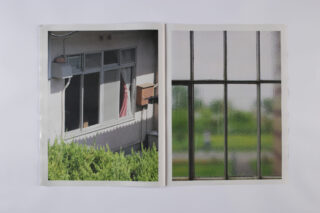 In einem offenen Buch sind zwei Fotos zu sehen: Das linke zeigt ein Gebäudefenster mit Vorhängen und Grünpflanzen, das rechte ein strukturiertes Fenster mit einer verschwommenen Außenansicht.