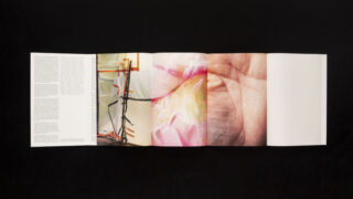 Ein gefaltetes Heft wird aufgeschlagen präsentiert und zeigt Seiten mit dichtem Text, abstrakter Kunst, einer Nahaufnahme einer Blume, einer Nahaufnahme einer Palme und einer leeren Seite, alles vor einem schwarzen Hintergrund.