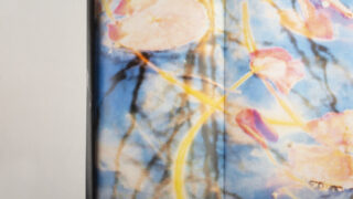 Eine Nahaufnahme eines Stoffes mit einem farbenfrohen abstrakten Blumendruck in Blau-, Rosa- und Gelbtönen neben einer schlichten weißen Oberfläche.