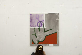 Eine Person mit langen Haaren und einem Haargummi betrachtet ein großes abstraktes Gemälde, das an einer weißen Wand hängt.