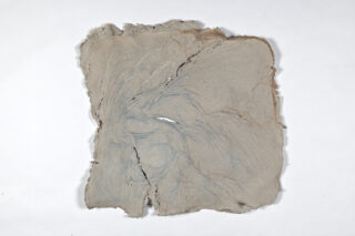 Quadratisches Blatt aus rauem, strukturiertem Papier mit ausgefransten Kanten, sichtbaren Rissen und dezenten blauen und beigen Markierungen auf einem schlichten weißen Hintergrund.