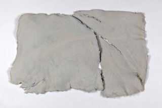 Ein großes, unregelmäßig geformtes Blatt hellgrauen handgeschöpften Papiers mit rauen Kanten und einem auffälligen diagonalen Riss auf der Oberfläche.