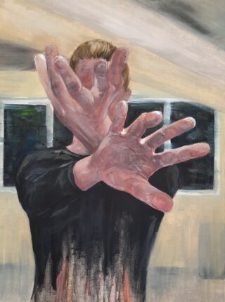 Eine Person steht in einem Raum mit erhobenen und vor dem Gesicht verschränkten Händen und Armen, wodurch ihre Gesichtszüge verdeckt werden. Im Hintergrund sind zwei rechteckige Fenster zu sehen.