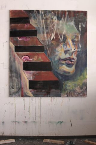 Neben einer Reihe dunkler, abstrakter Stufen mit rosa Details ist das Gemälde eines Gesichts in gedeckten Farben auf einer mit Spritzern übersäten Studiowand angebracht.