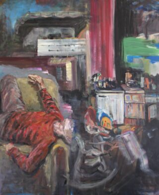 Eine Person in einem roten Pullover liegt auf einer Couch in einem überfüllten Raum, im Hintergrund sind verschiedene Gegenstände und ein unordentlicher Tisch zu sehen.