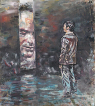 Ein Mann in einer braunen Jacke steht vor einem großen, teilweise abstrakten Gesicht, das sich aus einem dunklen, strukturierten Hintergrund abhebt.