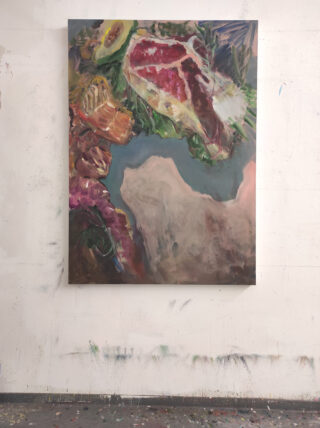 An einer weißen Wand in einem Atelier hängt ein farbenfrohes abstraktes Gemälde mit verschiedenen Formen und Texturen, vorwiegend in Rot-, Rosa-, Grün- und Beigetönen.