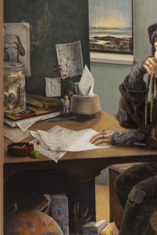 Eine Person sitzt an einem überfüllten Schreibtisch mit Papieren, Büchern, einem Modellglobus, Kunstbedarf, einer Taschentuchbox und einem Glas mit einem konservierten Objekt. An der Wand hängt ein Landschaftsgemälde.