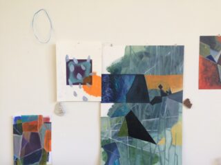 Abstrakte Gemälde mit geometrischen Formen und gedämpften Farben sind an einer weißen Wand befestigt, in deren Nähe kleine Objekte und eine blaue Schnur hängen.