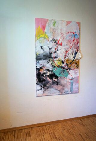 Ein farbenfrohes abstraktes Gemälde mit roten, gelben, schwarzen und weißen Elementen hängt an einer weißen Wand über einem Holzboden.