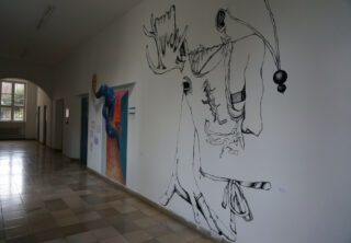 Ein Flur mit gefliesten Böden und Kunstwerken an den Wänden, darunter eine große abstrakte schwarze Strichzeichnung und eine bunte Figur in der Nähe mehrerer Türen.