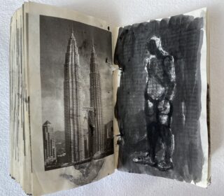 Ein offenes Buch zeigt auf der linken Seite ein Schwarzweißfoto von zwei Wolkenkratzern und auf der rechten Seite eine gemalte, abstrakte menschliche Figur in Graustufen.