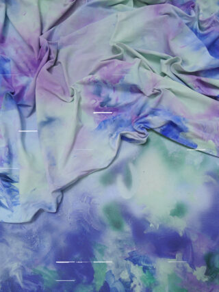 Ein pastellfarbener Batikstoff in Lila-, Grün- und Blautönen ist über eine ähnlich gefärbte bemalte Oberfläche mit schwachen horizontalen weißen Linien drapiert.