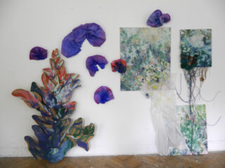 Kunstinstallation aus gemischten Medien an einer weißen Wand mit abstrakten Pflanzenformen, zerknittertem lila Papier, strukturierten Gemälden und drapiertem weißem Stoff.