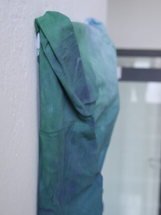 Ein Stück blau-grüner Stoff hängt über der Oberkante einer weißen Wand in der Nähe einer Glastür.