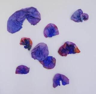 Zehn Stücke zerknülltes, mehrfarbiges Seidenpapier, hauptsächlich blau und violett, sind auf einem weißen Hintergrund verstreut.