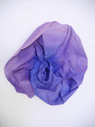 Ein Stück violetter Stoff ist locker gerafft und vor einem weißen Hintergrund drapiert, wodurch Falten und eine abstrakte, blumenähnliche Form entstehen.