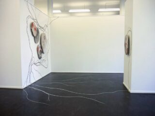 Kunstinstallation mit organischen, runden Formen auf weißen Wänden mit schwarzen und weißen Linien, die sich über die Wände und den Boden in einem Galerieraum mit dunklem Bodenbelag erstrecken.