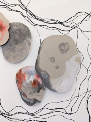 Drei organische, steinähnliche Formen in Grau-, Weiß- und Rottönen sind auf einem weißen Hintergrund mit schwarzen Wellenlinien und abstrakten Mustern überlagert.