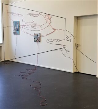 Großes Wandkunstwerk einer Person, die einen Rahmen hält, mit zwei Fotos und einer in das Kunstwerk integrierten roten Kordel, ausgestellt in einem minimalistisch weißen Raum mit geschlossener Tür.