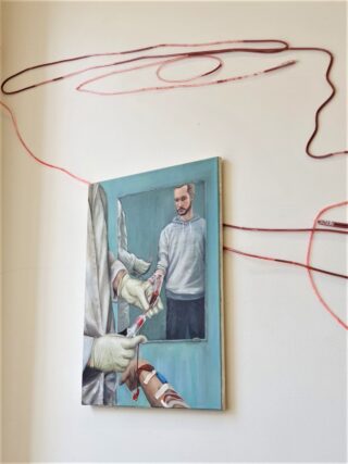 An einer Wand hängt das Gemälde eines Mannes, der sich in einem Spiegel spiegelt. Um und über dem Kunstwerk sind spiralförmig rote Röhren angeordnet, von denen einige mit dem Gemälde verbunden zu sein scheinen.