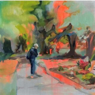 Eine Person steht auf einem geschwungenen Weg in einem Park, umgeben von Bäumen und buntem Laub, und blickt auf etwas in ihren Händen hinunter.