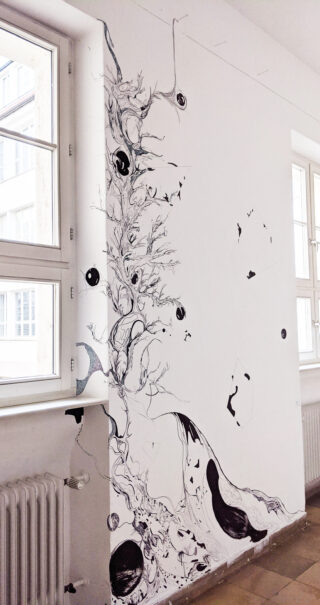 Ein schwarzes abstraktes Wandbild mit wirbelnden Linien, organischen Formen und Augen schmückt eine weiße Wand zwischen zwei großen Fenstern in einem hell erleuchteten Raum.