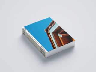 Ein Stapel Zeitschriften mit einem Titelbild einer Dachecke vor einem klaren blauen Himmel, platziert auf einer schlichten hellen Oberfläche.