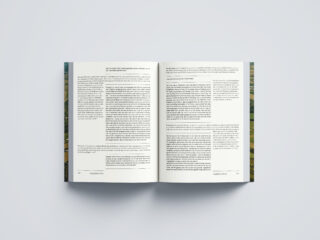 Ein offenes Buch liegt flach auf einer hellgrauen Oberfläche und zeigt zwei Seiten voller schwarzer Textblöcke und breiter Ränder.