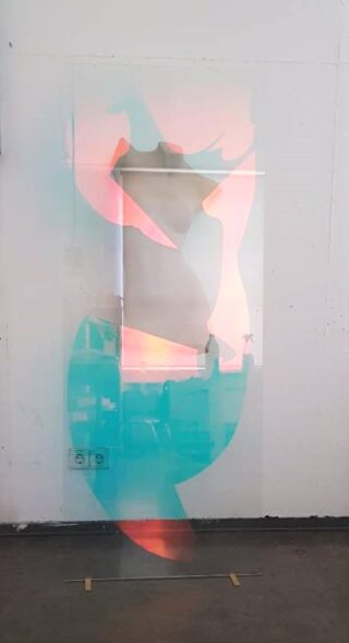 Eine durchscheinende Tafel mit abstrakten rosa und blauen Formen steht aufrecht vor einer weißen Wand in einem Raum im Industriestil.