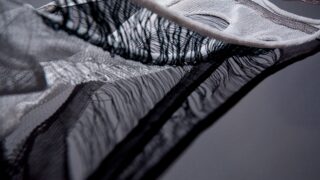 Nahaufnahme eines transparenten, locker gewebten schwarz-weißen Stoffes mit sichtbaren Fäden und offenen Flächen, die abstrakte Linien und Schatten erzeugen.