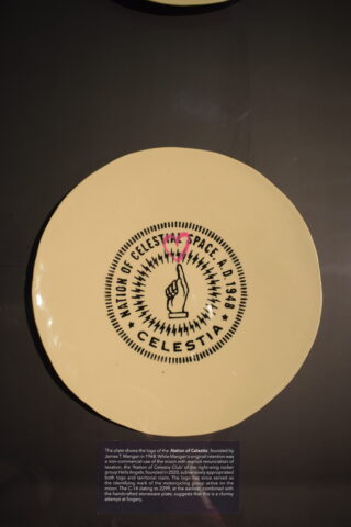 Ein runder Keramikteller mit dem Logo „Nation of Celestial Space“, einer zeigenden Hand und der Jahreszahl 1949 in der Mitte.