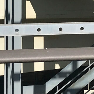 Sonnenlicht wirft Schatten von Metallgeländern und Balken auf eine Wand in der Nähe einer Treppe und erzeugt so geometrische Muster.