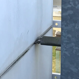 Eine Nahaufnahme einer Metallhalterung, die zwei große weiße Platten mit einem daran befestigten Metallträger sichert, aus einem Winkel gesehen.