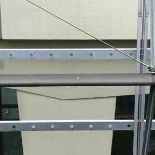 Eine Nahaufnahme von Metallgeländern und Stützstangen vor einer beigen Wand mit rechteckigen architektonischen Details.