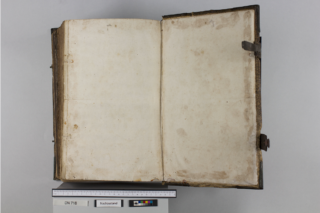 Ein altes, aufgeschlagenes Buch mit leeren, vergilbten Seiten liegt flach. Unter dem Buch befinden sich eine Skala und ein Etikett mit der Aufschrift „DN 718“ und „Nachzustand“.