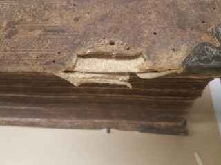 Nahaufnahme eines alten, abgenutzten Buches mit beschädigtem, zerrissenem Ledereinband und sichtbaren Metalleckenschützern.