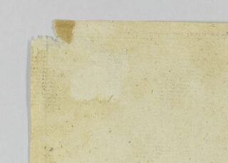 Eine Nahaufnahme der oberen linken Ecke eines vergilbten, beschädigten Papiers mit einer eingerissenen Kante und sichtbaren Flecken vor einem weißen Hintergrund.
