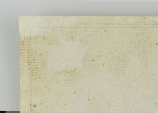 Eine Nahaufnahme der oberen linken Ecke eines vergilbten, strukturierten Blattes Papier mit schwachen Markierungen und einigen sichtbaren Abnutzungserscheinungen.